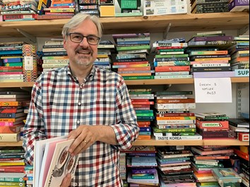 Man standing in front of bookshelves full of stacks of books