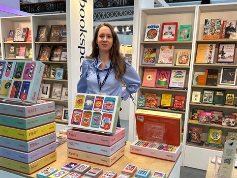 Woman at a trade show stand surrounded by books and games